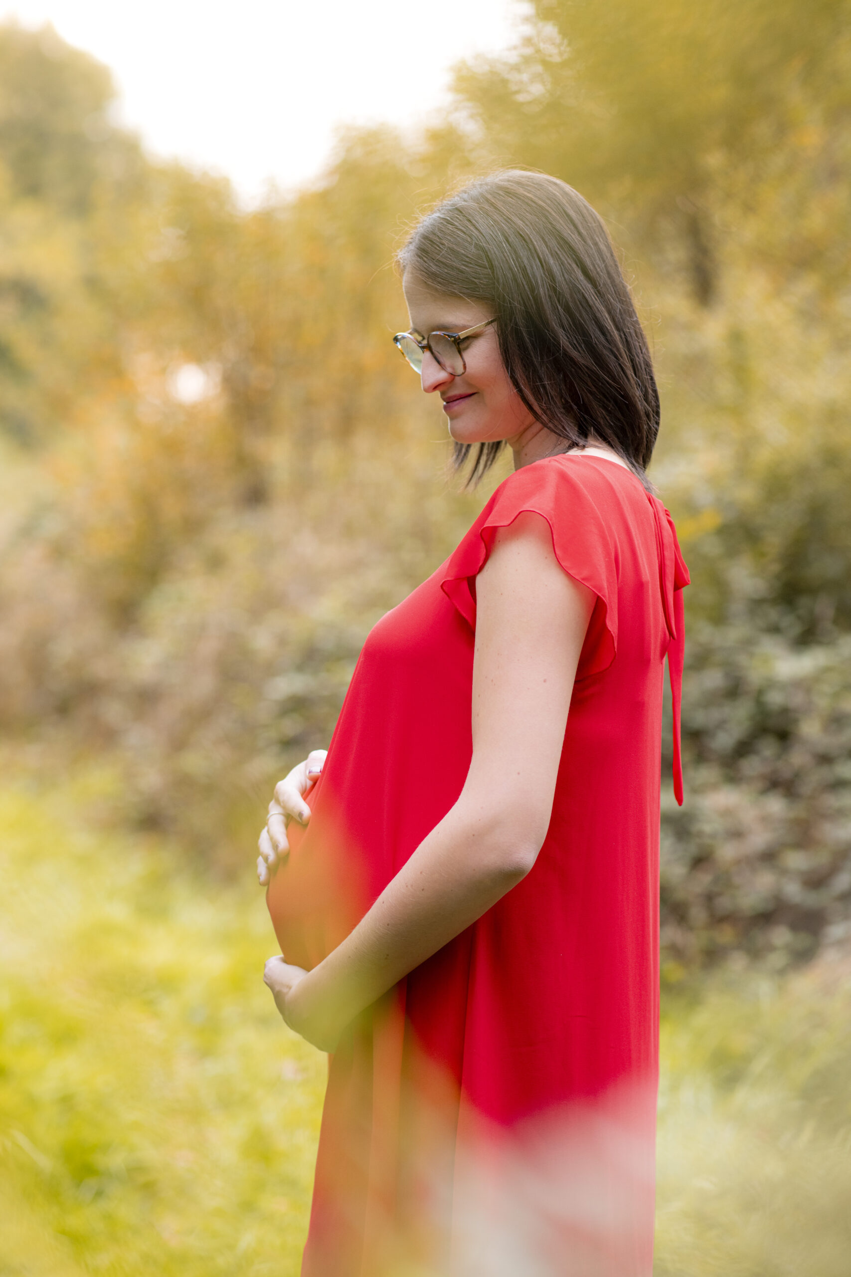 femme enceinte avec une robe rouge qui sourit en regardant son ventre