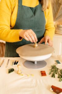 Artisan stamping clay on a pottery wheel with tools and herbs around.